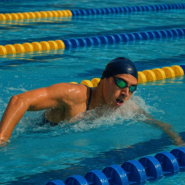 A swimmer is captured mid-stroke in a vibrant outdoor pool, where blue and yellow lane dividers create a rhythmic pattern on the water's surface.